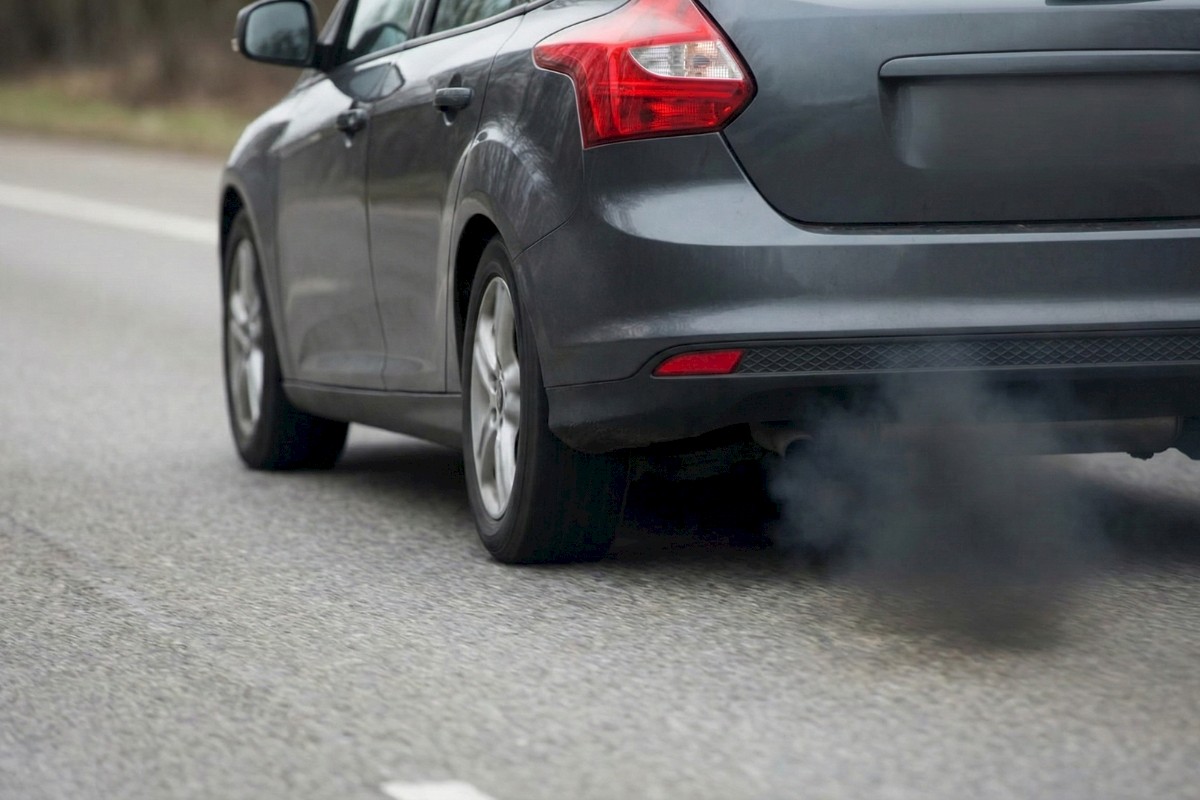 Une voiture émettant une épaisse fumée noire par son pot d'échappement en roulant.