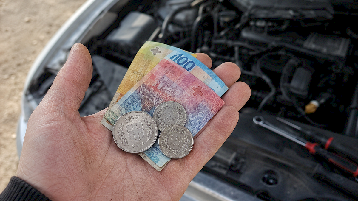 De la monnaie dans une main devant un moteur de voiture.